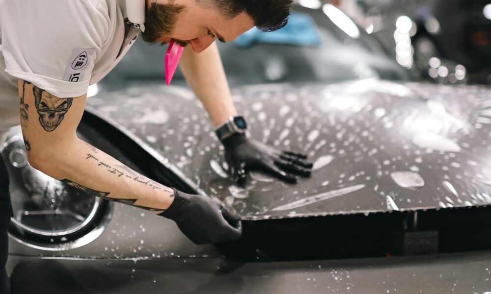 Man applying protective film to a sports car hood in an auto detailing workshop.