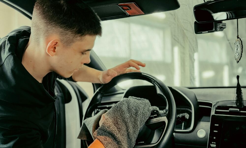 Young man polishing car steering wheel with cloth, ensuring clean interior.